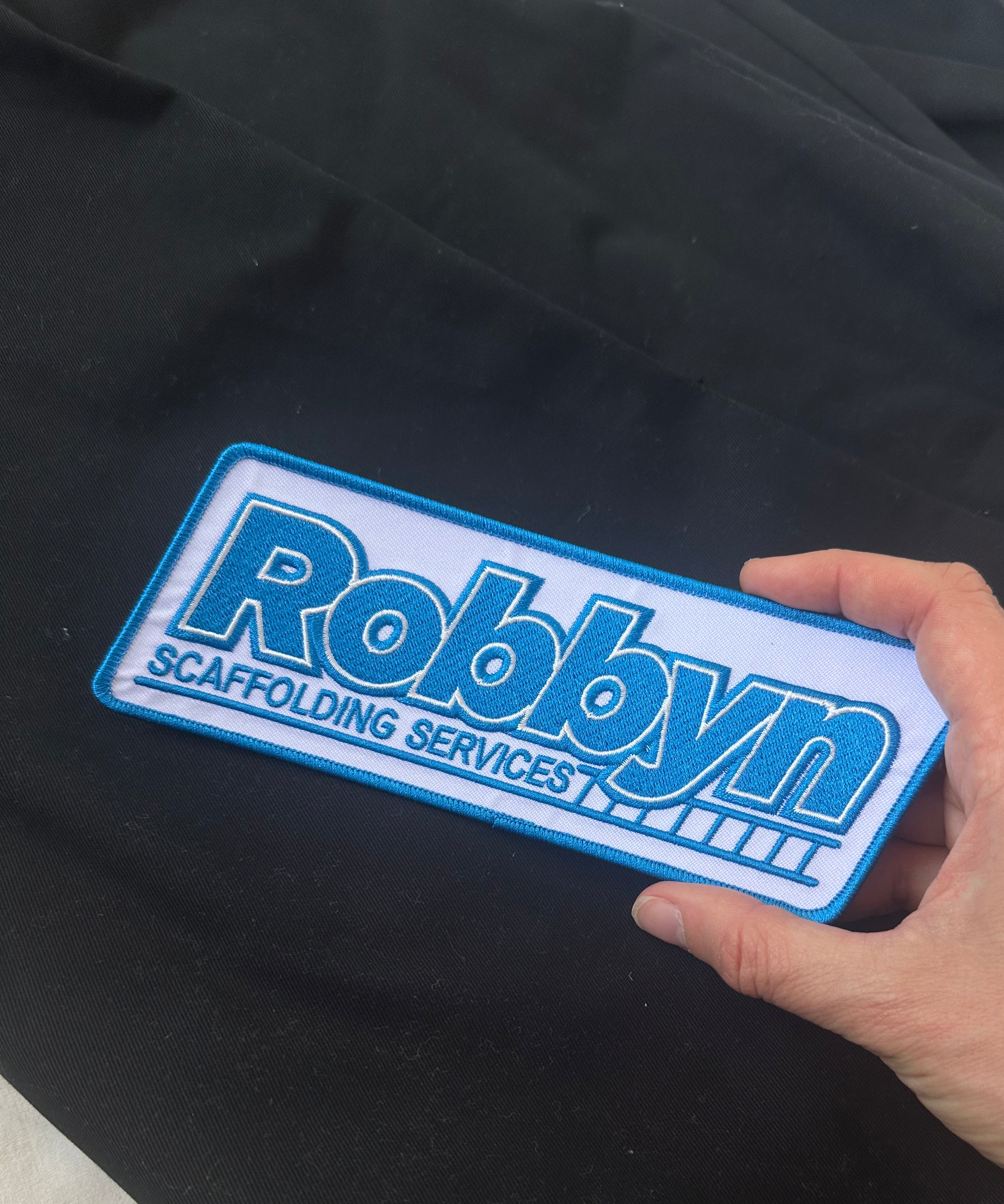 Hand holding a blue and white patch with 'Robbyn'